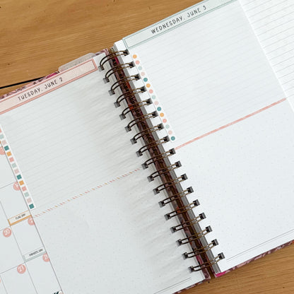 an open spiral-bound notebook with a blank page, resting on a wooden surface.
