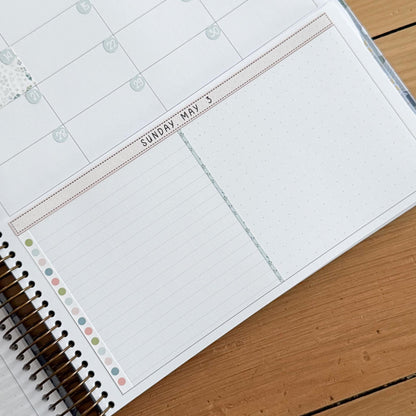 a spiral-bound notebook with a blank page and a calendar page with the date "SUNDAY MAY 3" written on it.